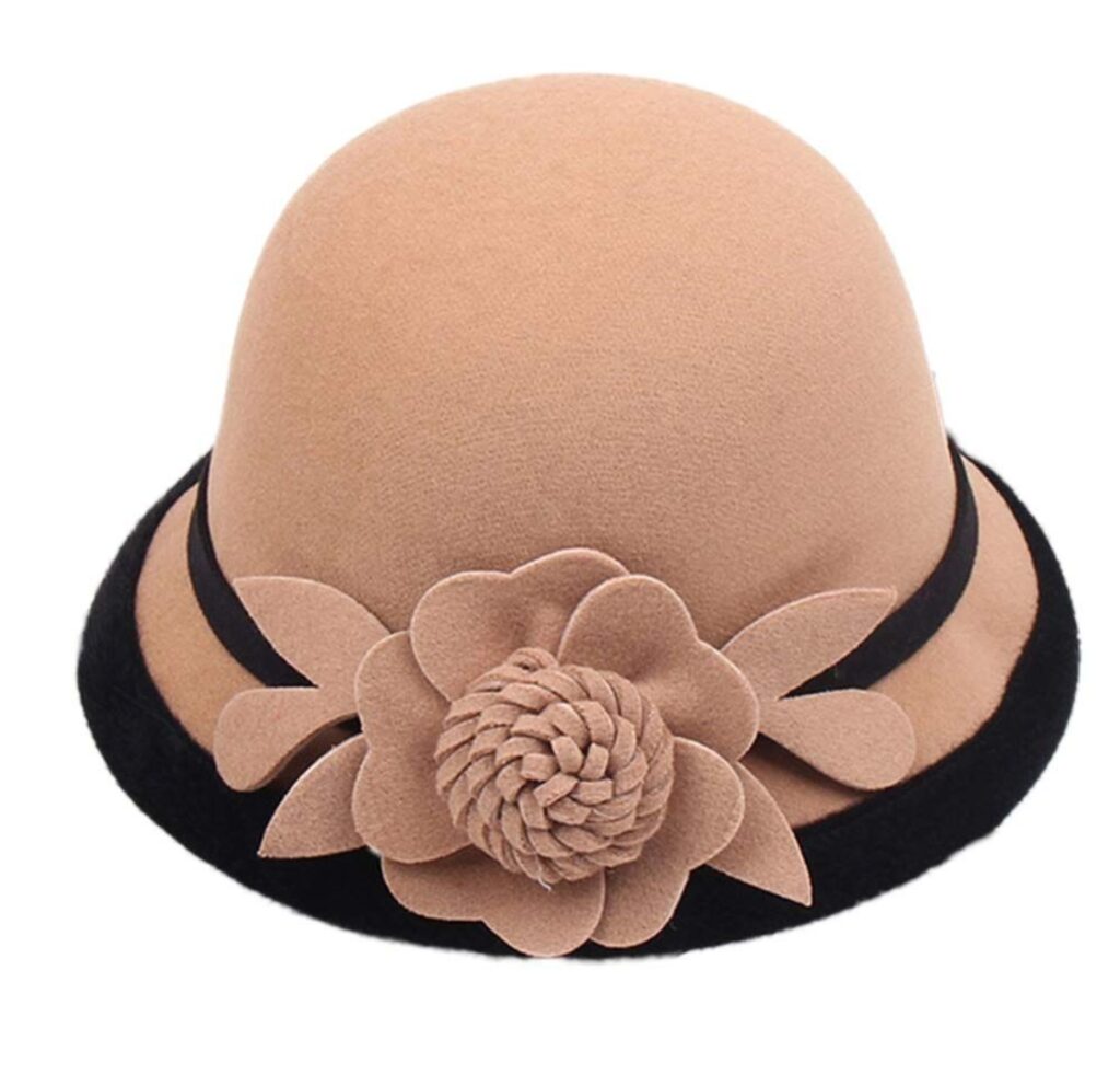 A stylish beige cloche hat with a black band and a large beige fabric flower on the side.