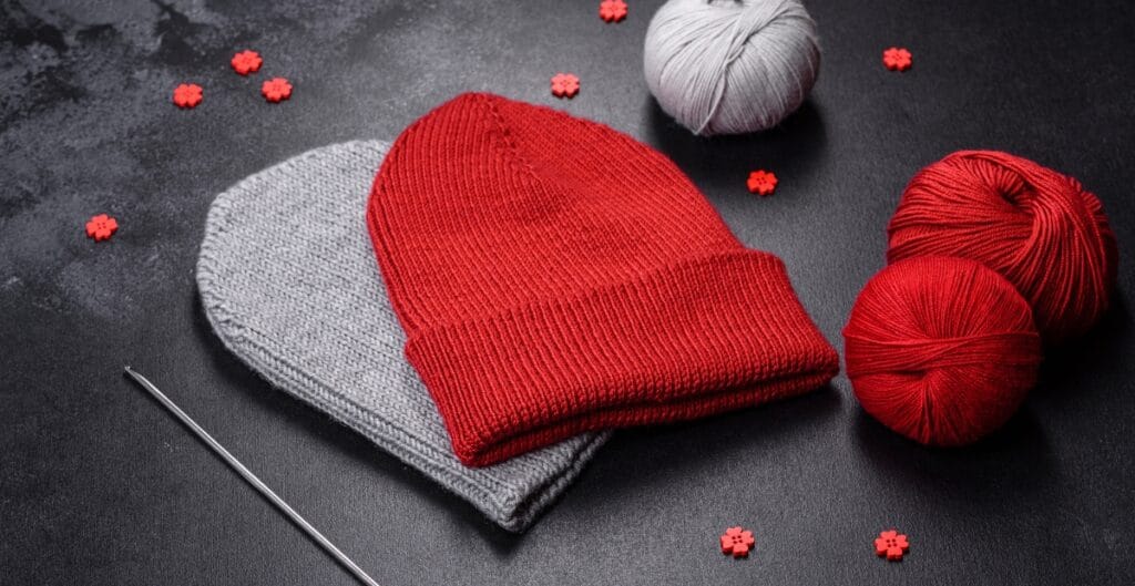 Red and light grey knit beanies with balls of yarn and a knitting needle