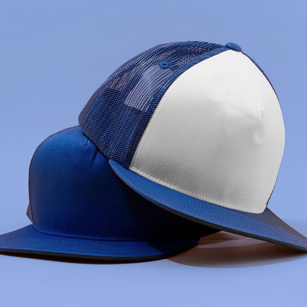 A blue and white trucker cap with a white front panel and blue mesh back, placed on a flat surface against a light blue background.