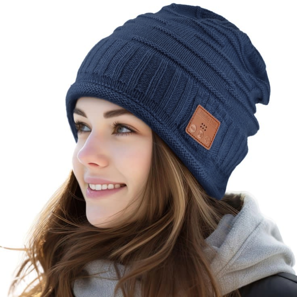 A woman wearing a dark blue knit beanie with a small brown leather patch on the side, showcasing a modern Bluetooth-enabled beanie.
