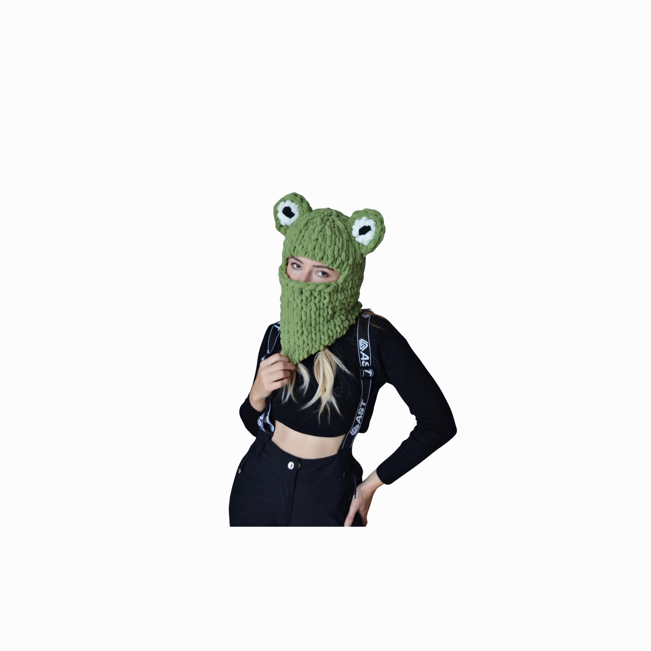 A person wearing a chunky green knitted balaclava with frog-like eyes on top, covering the head and neck while leaving the eyes visible.