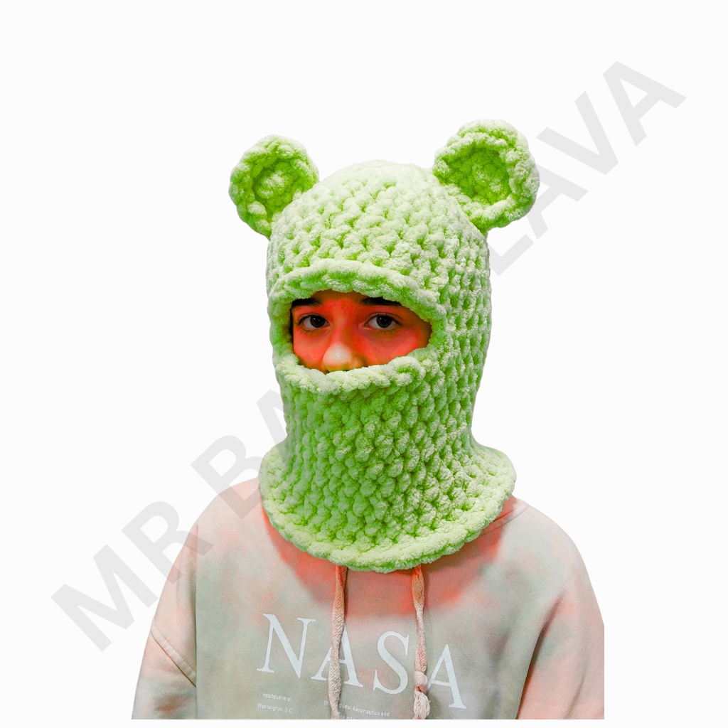 Lime-green knitted balaclava with two rounded ear-like protrusions and a large eye opening, worn by a person.