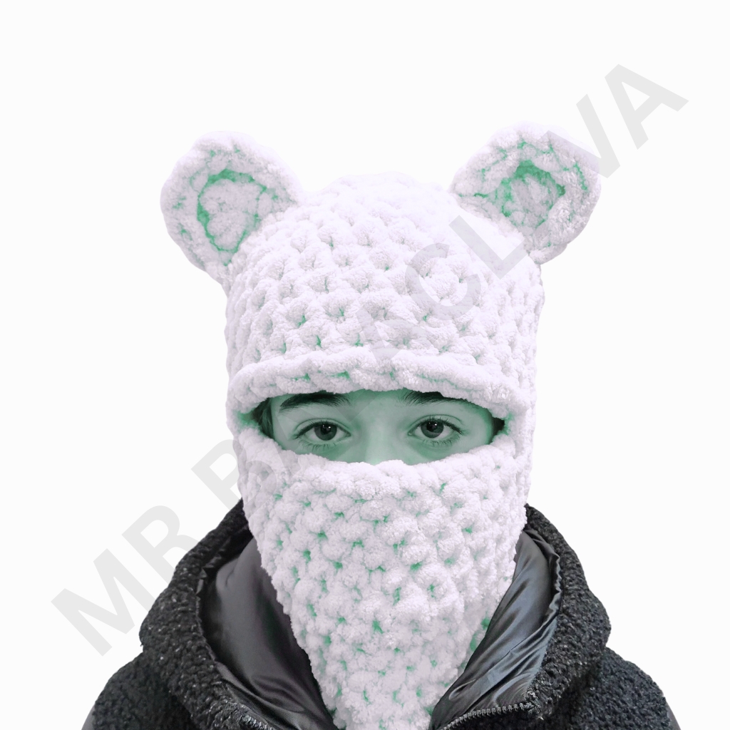 White crochet balaclava with knit texture and two rounded ear-like protrusions, worn over the head with eye and neck openings.