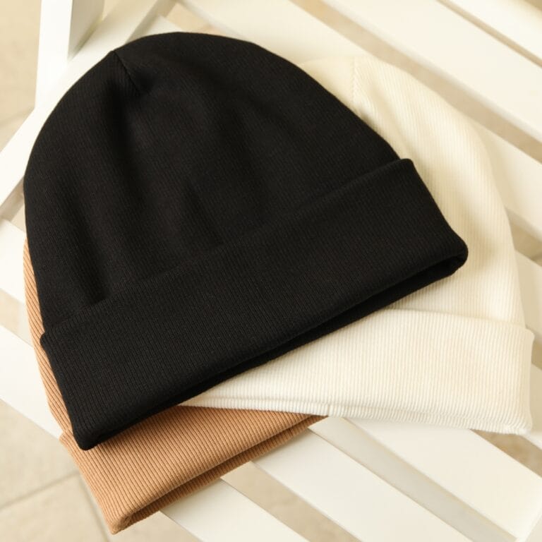 Stack of three ribbed knit beanies in black, white and camel with turned-up cuffs