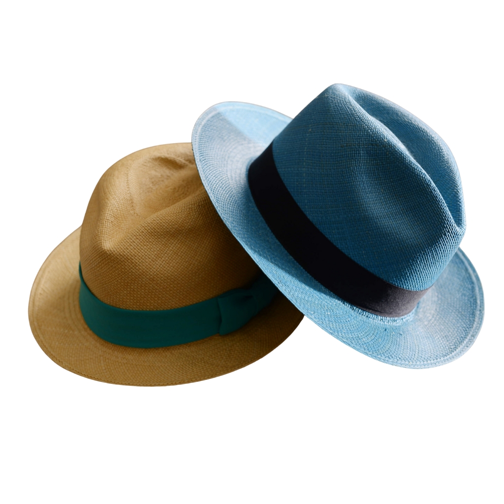 "Two Panama hats stacked together: one natural straw hat with a green band and one light blue straw hat with a black band, set against a white background."

