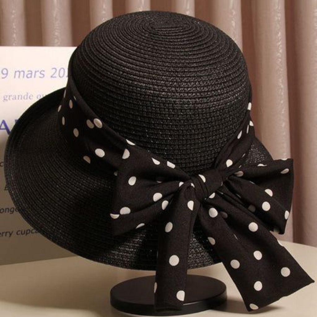 A black woven hat with a wide brim, featuring a large black ribbon tied into a polka-dotted bow with white dots.