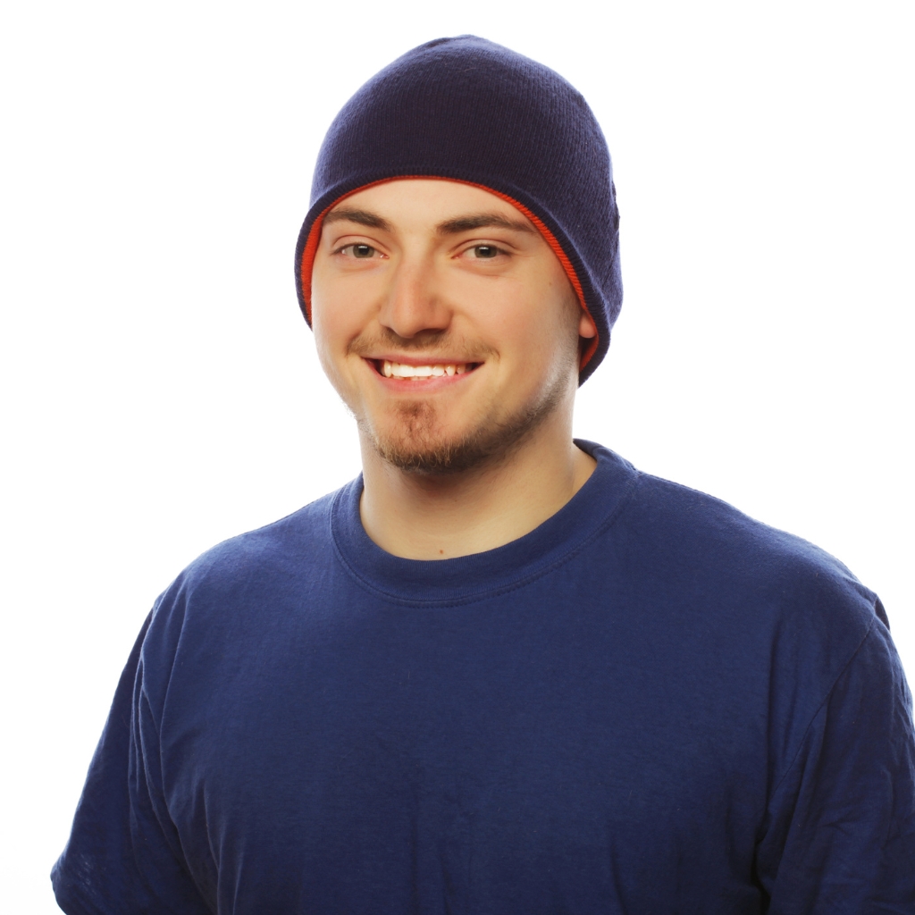 A smiling man wearing a dark blue beanie and a matching blue T-shirt, posed against a plain white background.