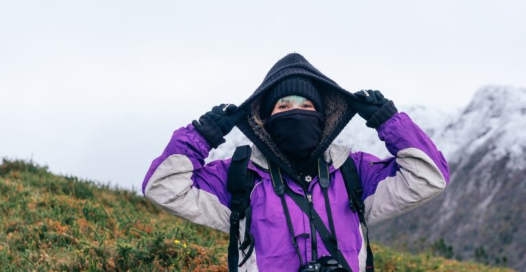 Wanderer mit schwarzer Sturmhaube und lila Jacke im Freien, der zeigt, wann die Sturmhaube gewaschen werden muss und wie sie zu pflegen ist.