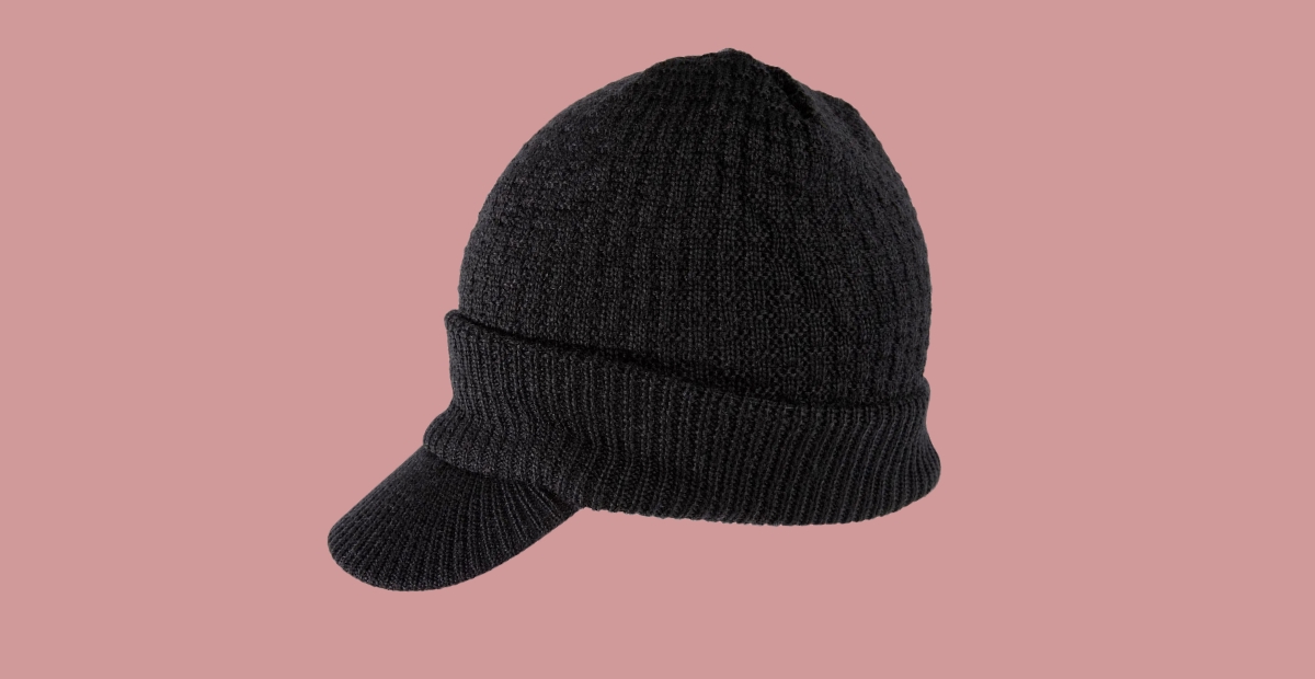 Eine schwarze Strickmütze mit Schirm vor einem gedeckten rosa Hintergrund.