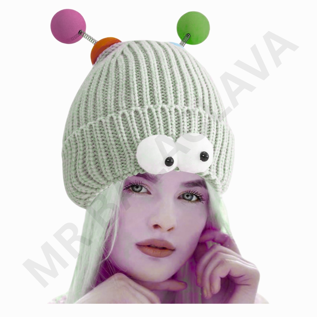 A person wearing a chunky, light-gray knitted beanie with two large white googly eyes on the front and colorful antennae with pink, orange, and green spheres extending from the top.