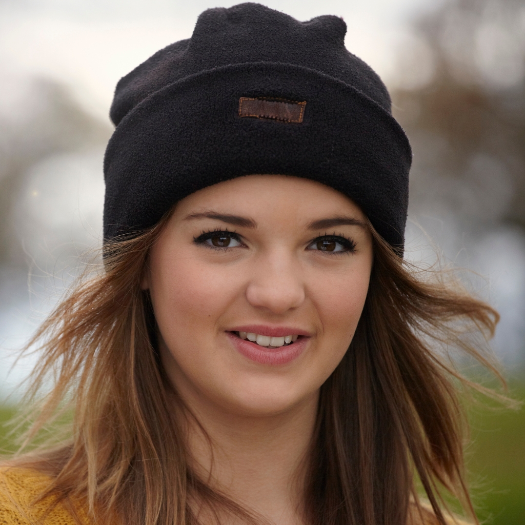 Primer plano del retrato de una mujer sonriente con un gorro negro de punto en un entorno al aire libre.