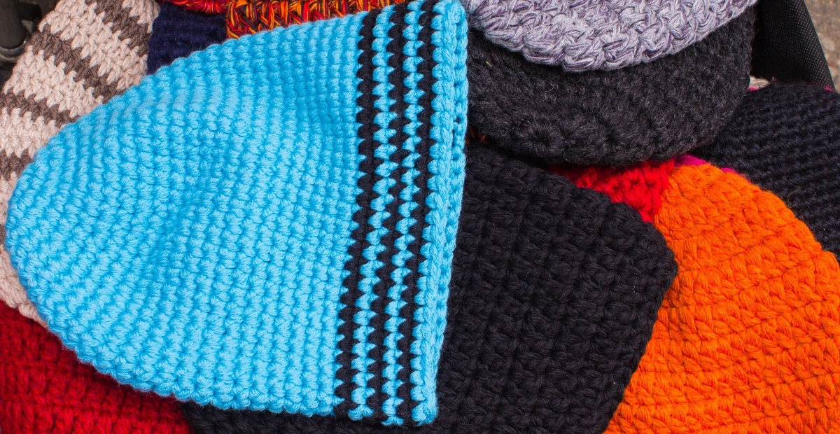 Ein Stapel gestrickter Mützen in verschiedenen Farben, darunter eine auffällige hellblaue Mütze mit schwarzen Streifen, die strukturierte Maschen aufweist.