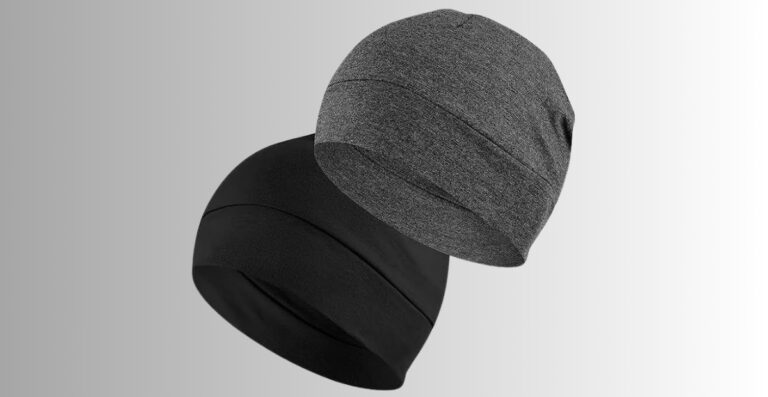 Zwei weiche, gestrickte Helmunterziehmützen in Schwarz und Grau, die sich vor einem hellgrauen bis weißen Hintergrund mit Farbverlauf überlagern.