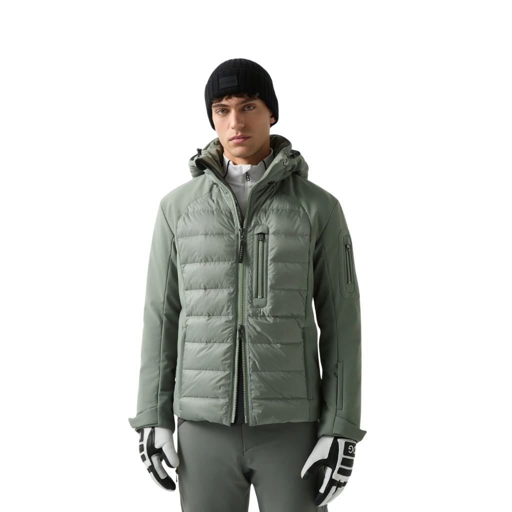 A man wears a light green insulated ski jacket with a hood, paired with dark green pants, gloves, and a black beanie. He stands against a plain white background.
