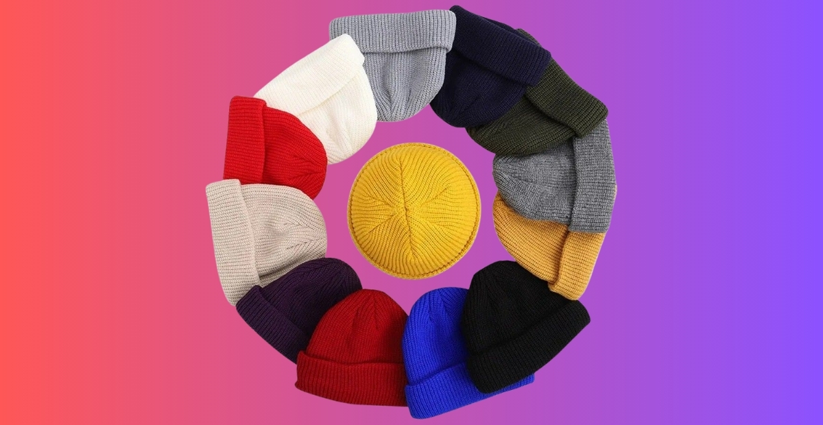 Eine kreisförmige Anordnung von bunten Strickmützen in Rot, Creme, Grau, Marineblau, Senfgelb, Schwarz, Blau und anderen Farbtönen, angeordnet um eine leuchtend gelbe Uhrmütze auf einem rosa- bis violetten Farbverlaufshintergrund.