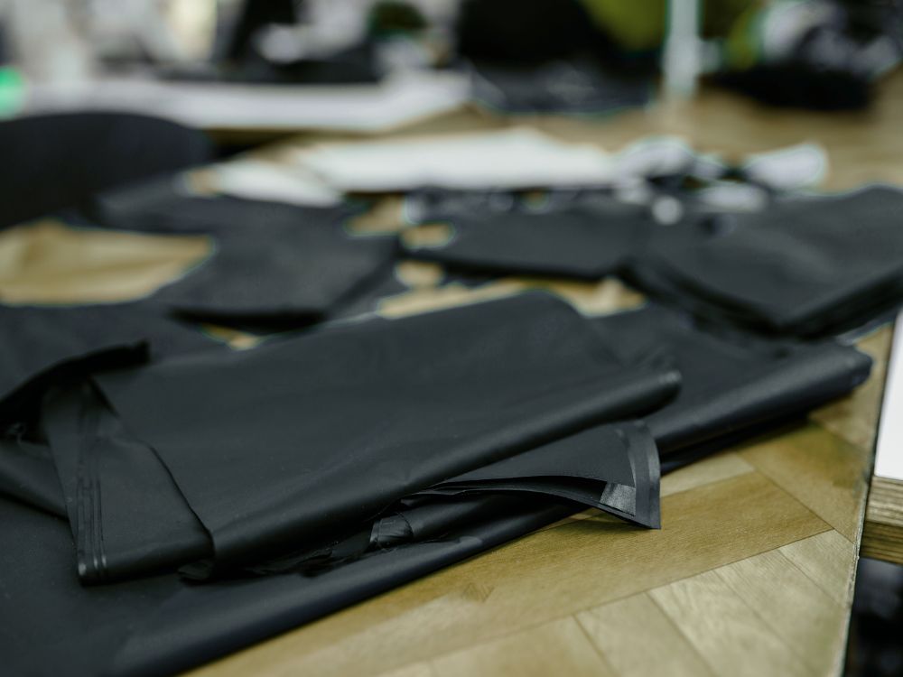 Skis and skiing jackets being manufactured; workers sew seams, inspect materials, and apply waterproof coatings on a factory floor.