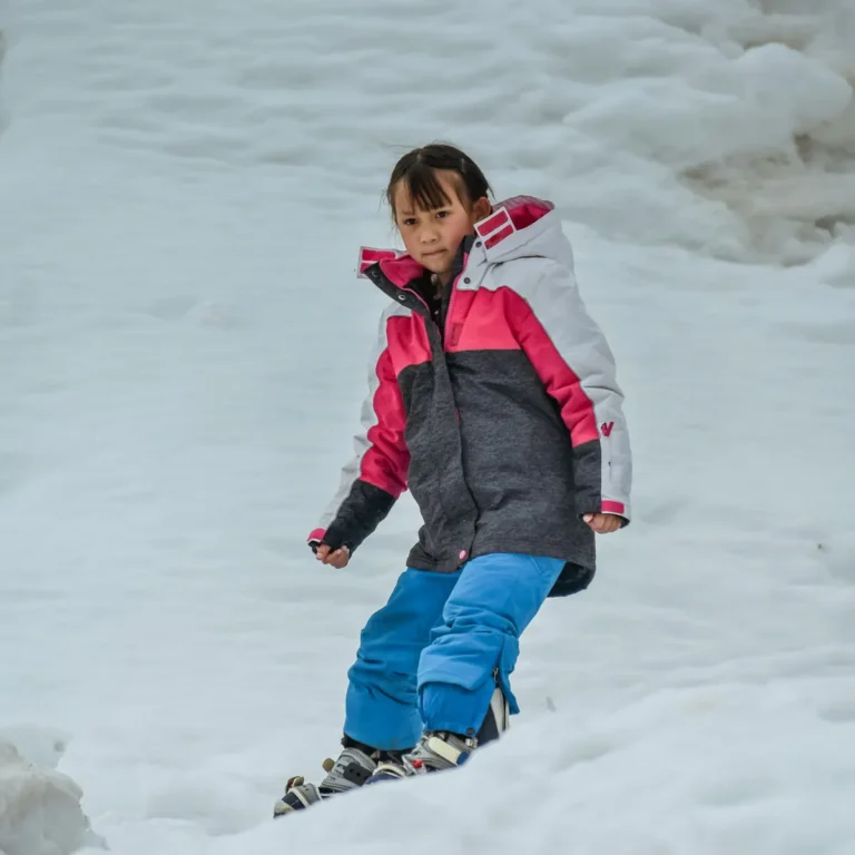 Girl in a pink and grey ski jacket and blue ski pants riding down a slope