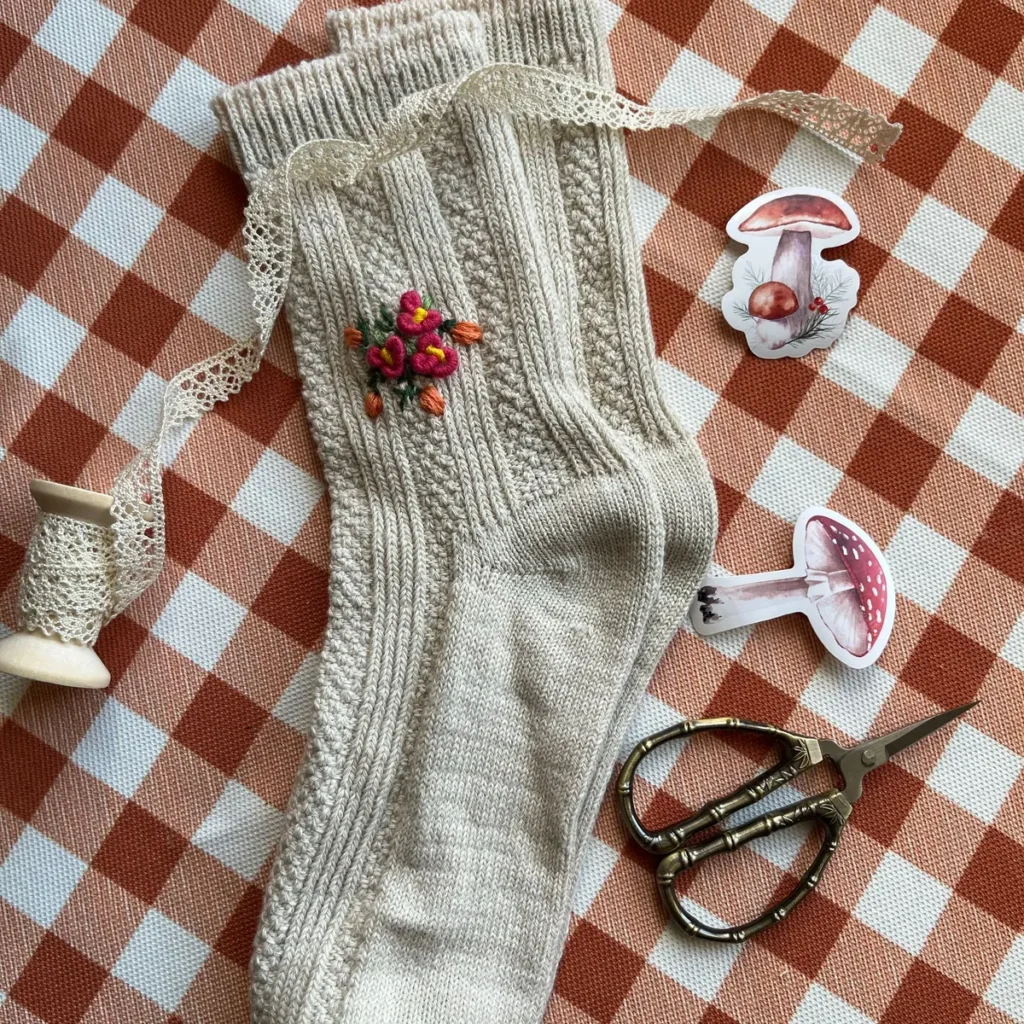 Chaussette crème à torsades posée à plat sur un tissu à carreaux avec de petits détails décoratifs