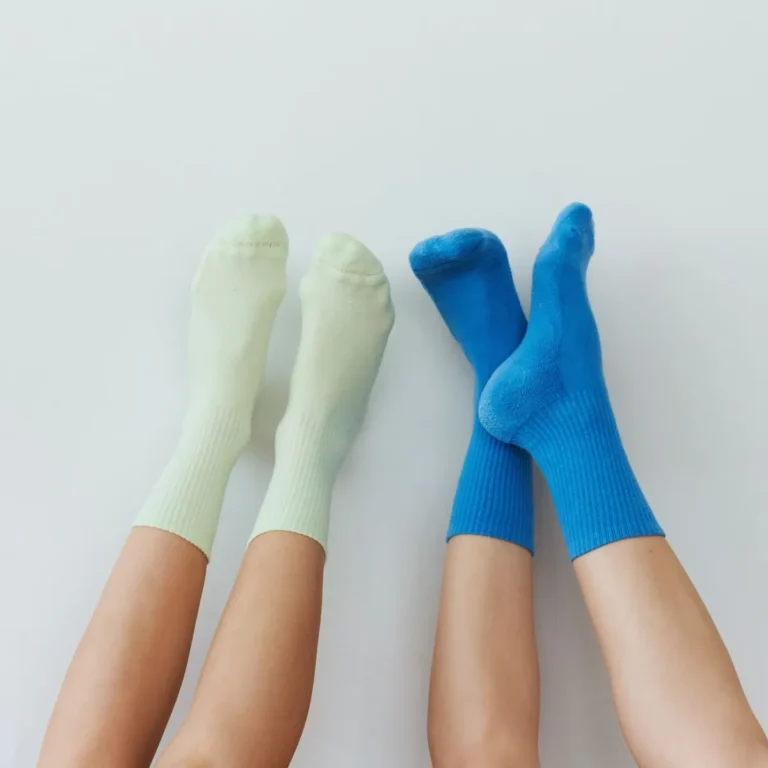 Two pairs of ribbed crew socks in pale green and bright blue, worn with legs resting on a white surface