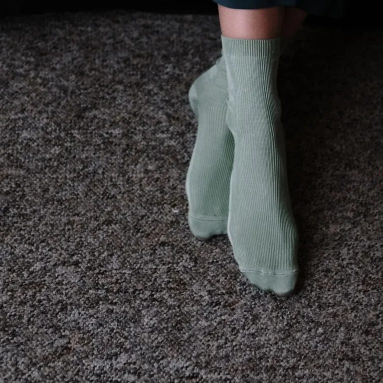 Sage green ribbed quarter socks worn on a grey carpet