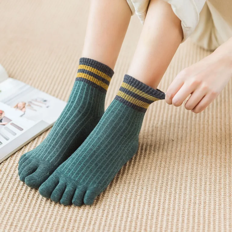 Person adjusting ribbed green toe socks with gold stripes on a woven mat