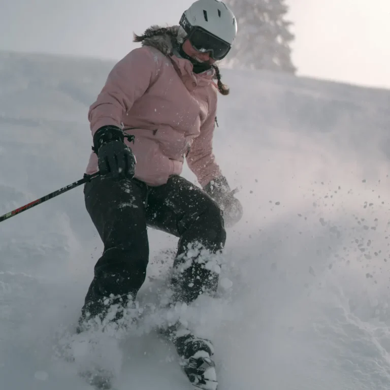 Skier in a pink ski jacket and black ski pants turning in fresh snow