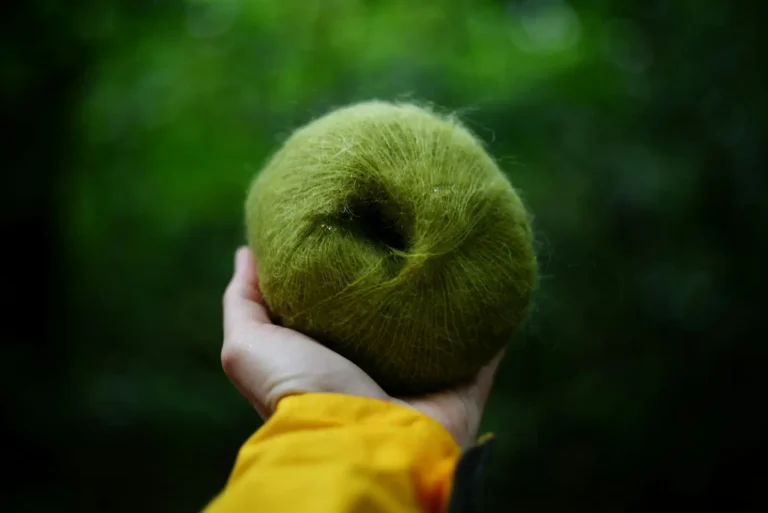 Hand holding a ball of fuzzy green yarn with a soft halo